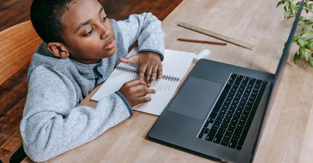 pexels-photo-5905702-5905702 From above of smart cute African American boy studying online with netbook while sitting at table with notebook and pencil