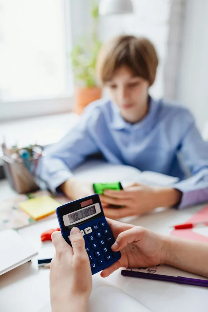 Teenager focused on math homework, using calculator at desk, indoors.
